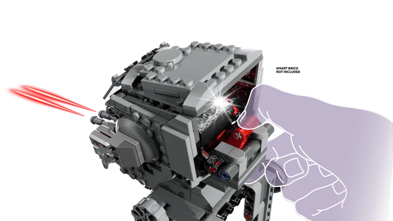 A hand inserting a 'Smart Brick' (not included) into the head of the Lego AT-ST walker, which emits red laser light effects from its cannons, highlighting interactive features.