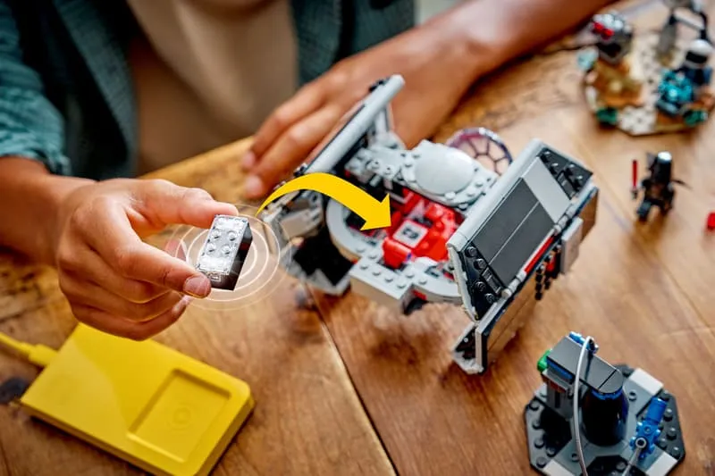 A person's hands carefully inserting the small, rectangular Smart Brick into an open compartment of Darth Vader's TIE Fighter.
