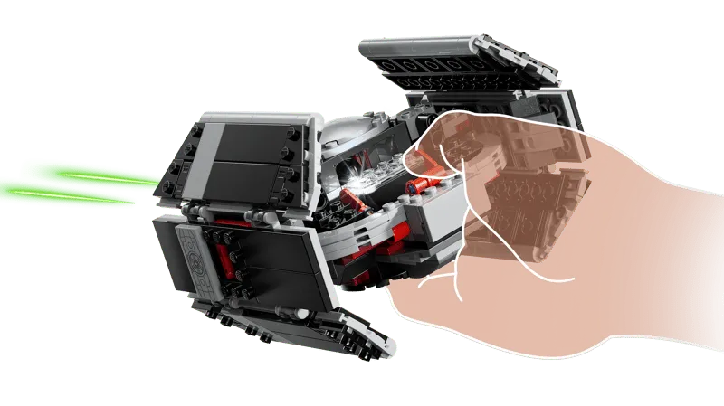 A hand holding Darth Vader's TIE Fighter, with its top panels slightly open, showing the internal smart brick slot and emitting green laser effects.