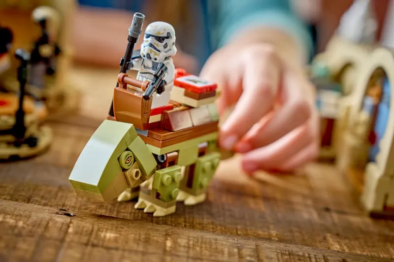 A child's hands playing with the Lego Dewback-like creature and the Sandtrooper minifigure from the Mos Eisley Cantina 75425 set.