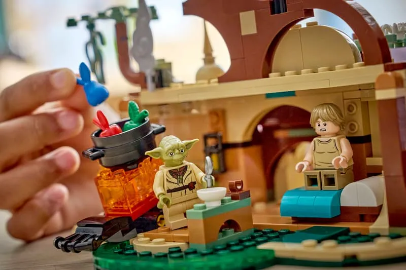 Close-up of a hand placing a colorful piece into Yoda's cauldron, with Luke Skywalker minifigure sitting nearby, from the Lego SMART Play™: Yoda's Hut and Jedi Training 75422 set.