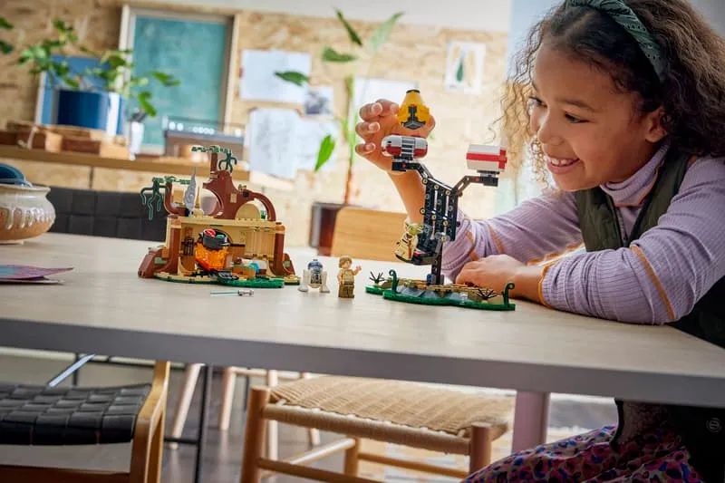 A young girl happily playing with the Lego SMART Play™: Yoda's Hut and Jedi Training 75422 set on a table, manipulating the training structure.