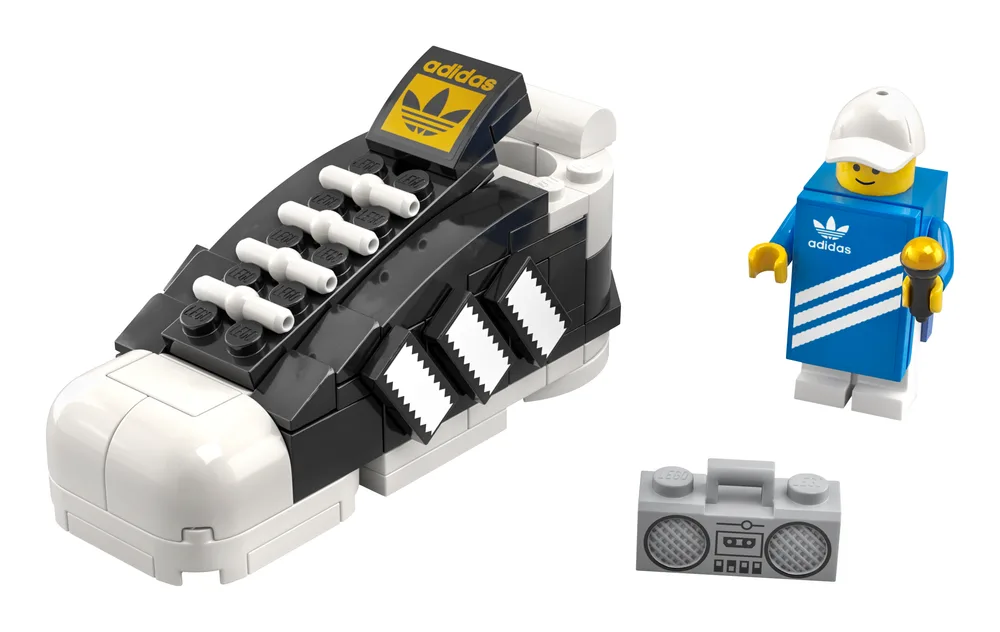 A LEGO-built black and white adidas Superstar sneaker with a white shell toe, alongside a blue-suited minifigure holding a golden microphone and a grey brick-built boombox.