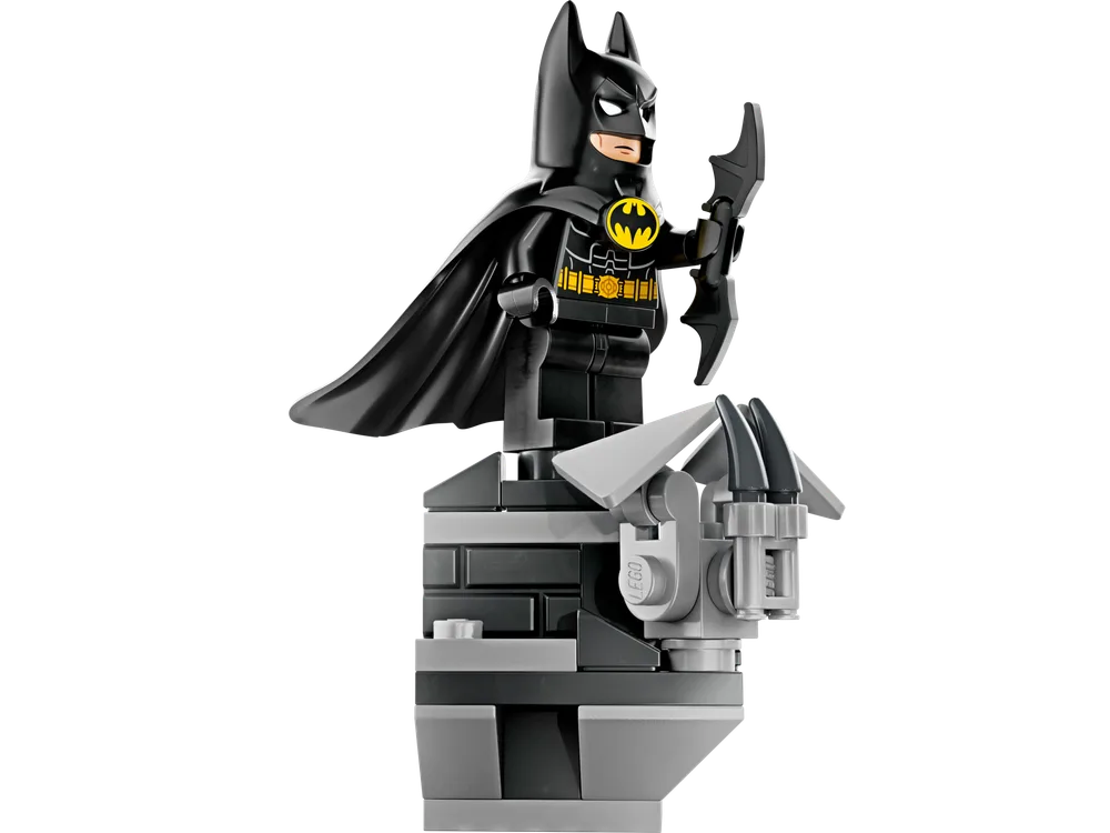 Close-up of a LEGO Batman minifigure with a black cape and batarang, standing on a dark grey, angular rooftop build.