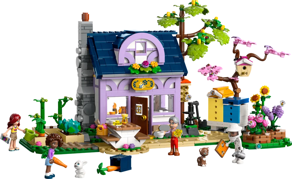 Full view of the LEGO Friends Beekeeper's House and Flower Garden set, showing the lavender house with a dark blue roof, a large tree, beehives, and minifigures in a lush green garden.