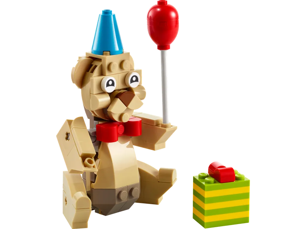 A tan brick-built bear in a party hat holds a red balloon, next to a small green and yellow striped gift.