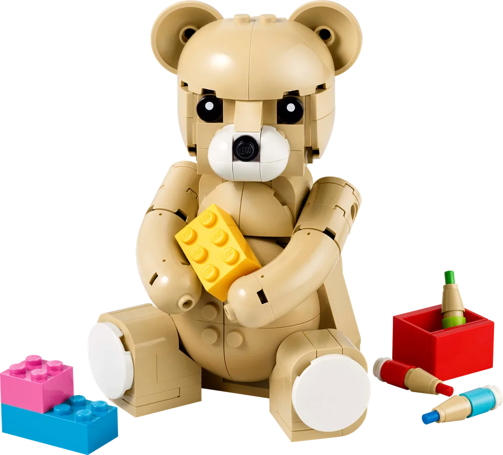 A LEGO teddy bear in tan, seated and holding a yellow 2x4 brick, surrounded by loose colorful LEGO bricks and coloring pens.