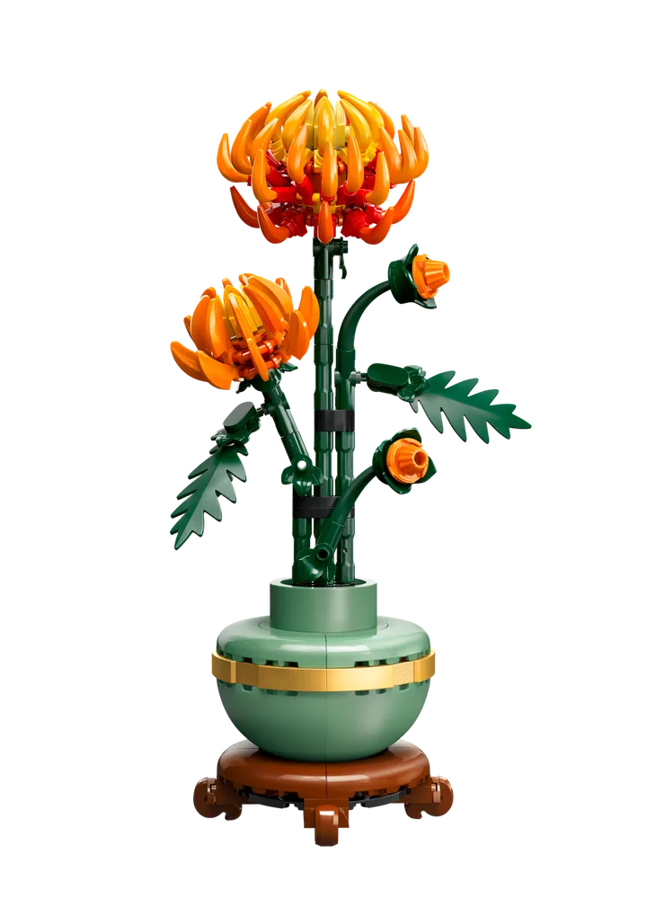 A vibrant LEGO chrysanthemum with orange and red petals stands tall in a dark teal pot with gold accents, set against a stark white background.