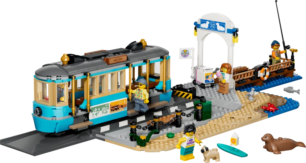 A fully assembled LEGO City Classic Beach Streetcar (60506) set with the teal tram, a sand-colored beach section, a white archway station, a wooden pier, and several minifigures enjoying beach activities. A sea lion and a fish are also present.