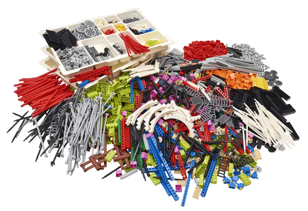 A large, diverse pile of LEGO bricks, primarily Technic elements, along with white sorting trays filled with smaller pieces and gears.