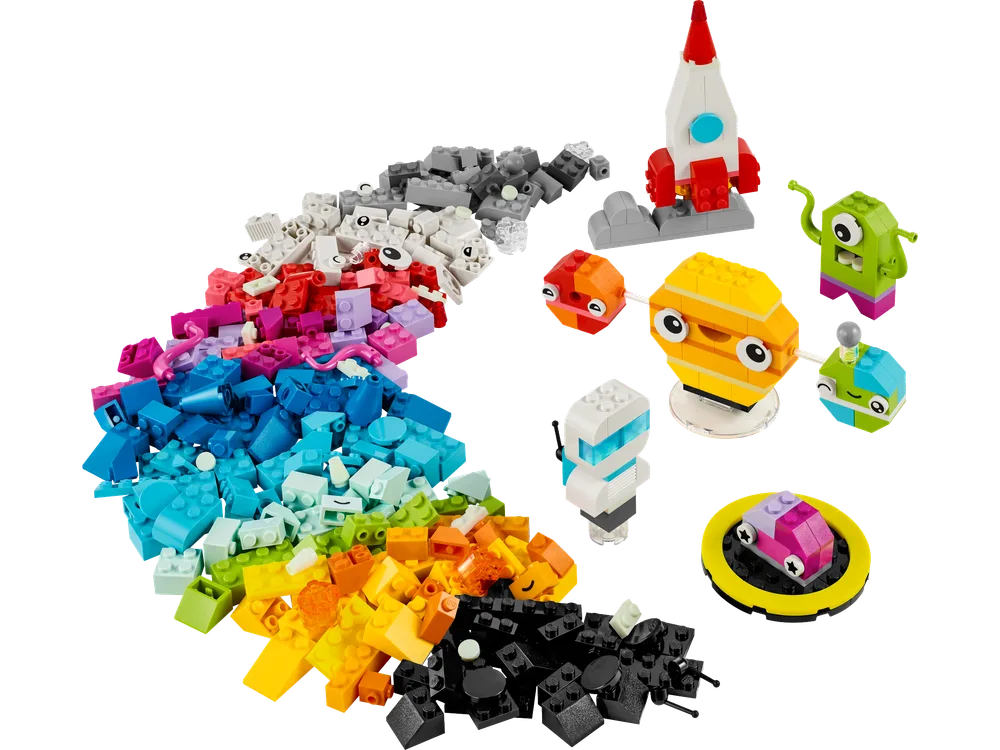 An overhead shot of all 450 LEGO Classic Space Planet building bricks, neatly sorted by color, forming a vibrant rainbow arc on a white background. Several completed space-themed models are arranged to the right, including a white and red rocket, a green alien, a large yellow planet with smaller orbiting planets, a grey robot, and a small purple flying saucer.