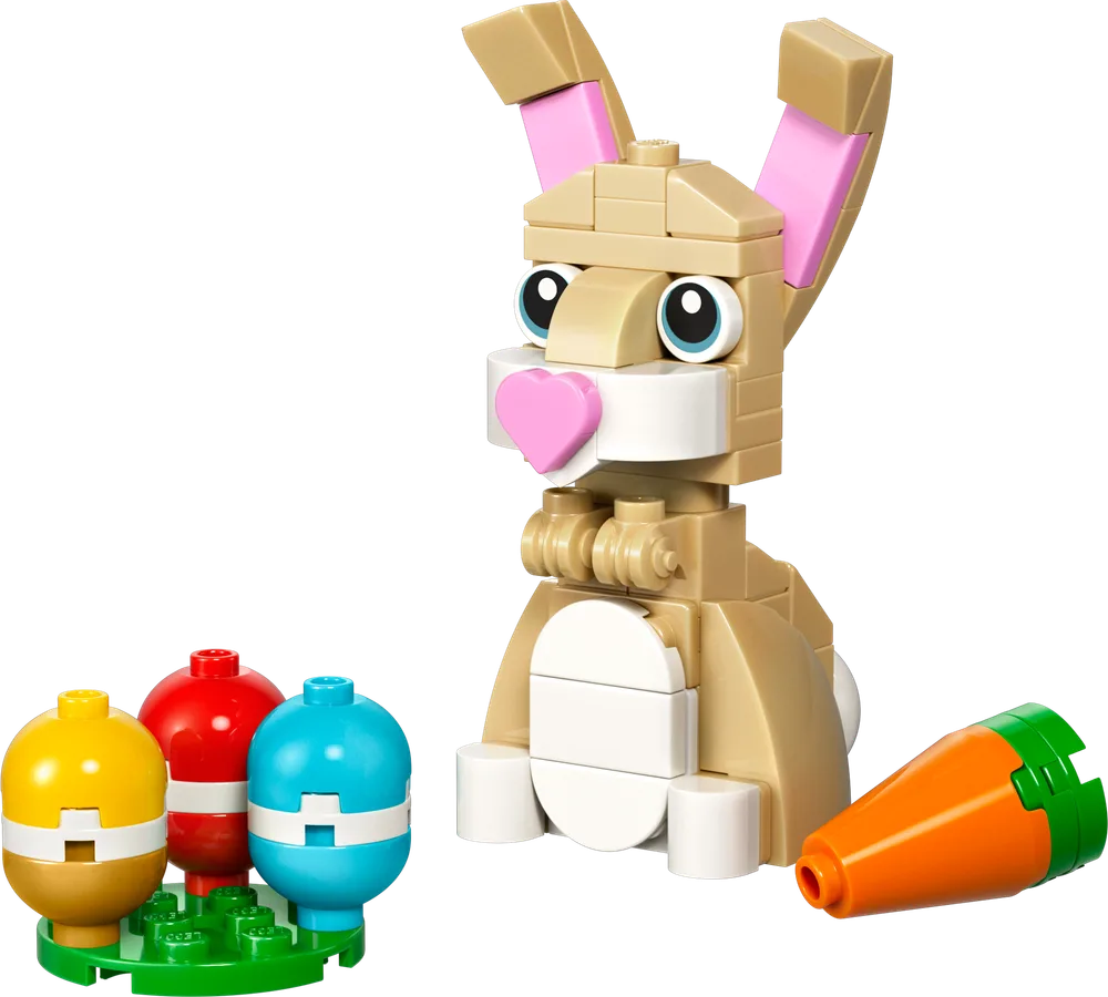 A tan LEGO brick-built bunny with pink ears and a heart-shaped nose, sitting next to three colorful Easter eggs on a green plate and a loose orange carrot.