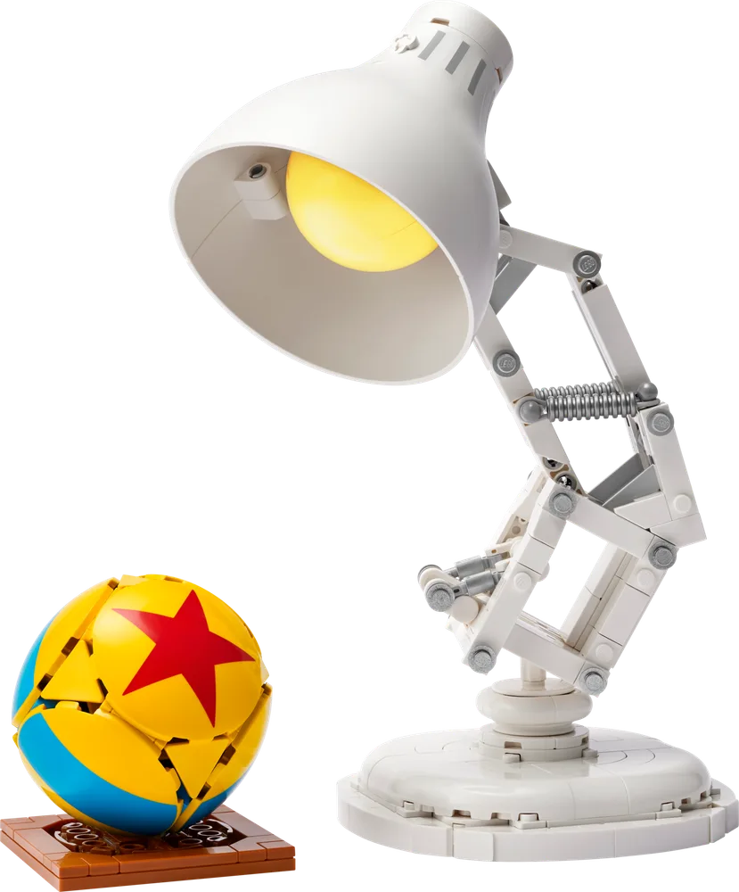 The LEGO Ideas Luxo Jr. lamp model with its light on, standing next to the segmented yellow and blue Luxo Ball with a red star, both on a white background.