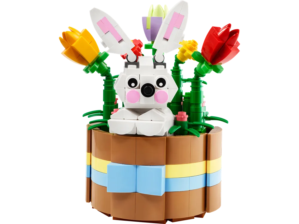 A LEGO build of a white rabbit sitting in a round, brown basket with yellow and blue stripes, surrounded by colorful red, yellow, and purple tulips with green stems.