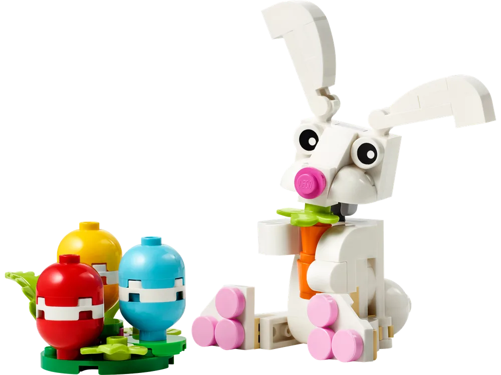 A white LEGO Easter bunny holding a green carrot sits next to three colorful Easter eggs (red, yellow, blue) on a green base.