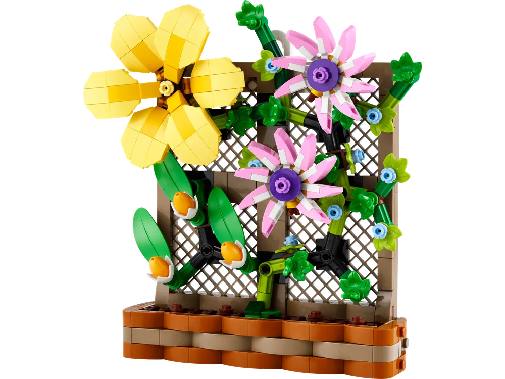 A close-up, front view of the LEGO Flower Trellis Display showing a large yellow flower, two pink flowers, and green vines with small blue and orange accents climbing a brown trellis structure, all set within a brown pot base.