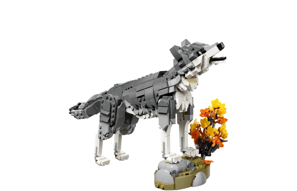 A gray LEGO wolf model stands on a rock formation with autumn-colored foliage, howling upwards.