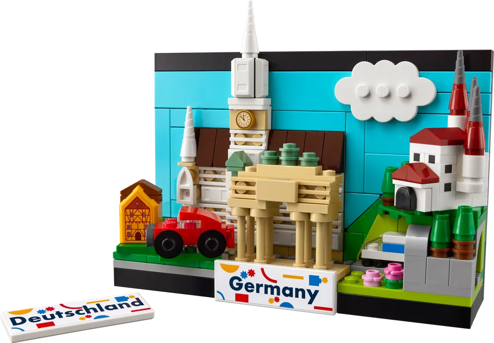 The fully assembled LEGO Creator Germany Postcard set, displaying iconic German landmarks like the Brandenburg Gate, a traditional half-timbered house, a church tower with a clock, and a red car, set against a blue sky background. The "Germany" printed tile rests at the front base.