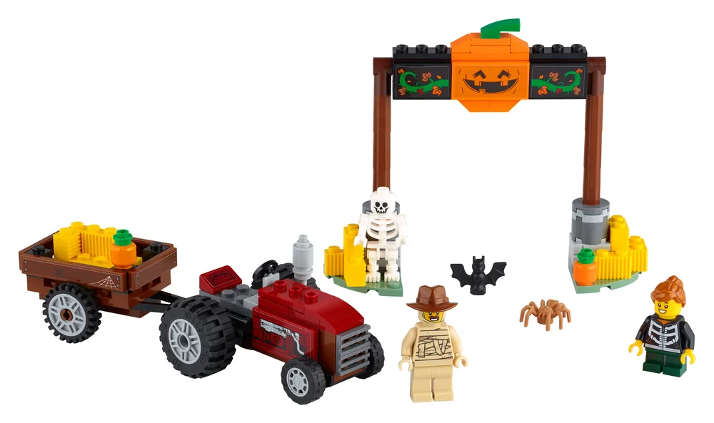 LEGO Halloween Hayride (40423) set with a red tractor, brown wagon, pumpkin arch, and three minifigures: a skeleton, a mummy, and a child in a skeleton costume, along with a bat and spider.