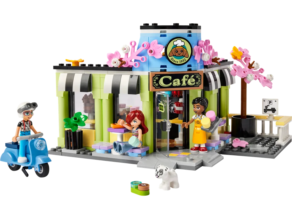 Front exterior view of the LEGO Heartlake City Cafe, featuring a lime green and black striped awning, blue circular rooftop element, and pink cherry blossom trees. Minifigures Liann, Paisley on a scooter, and the barista are visible, along with a dog.