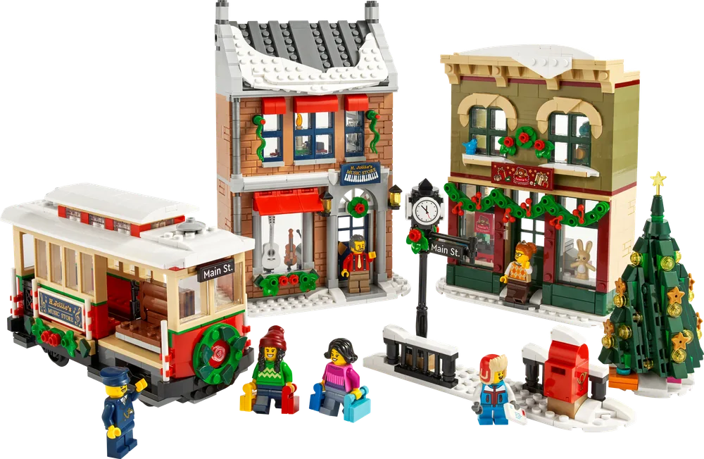 An overhead shot displaying the entire LEGO Holiday Main Street set, including two decorated buildings, a tram, a clock tower, a mailbox, and a Christmas tree, all on a white background. Minifigures are scattered throughout the snowy scene.