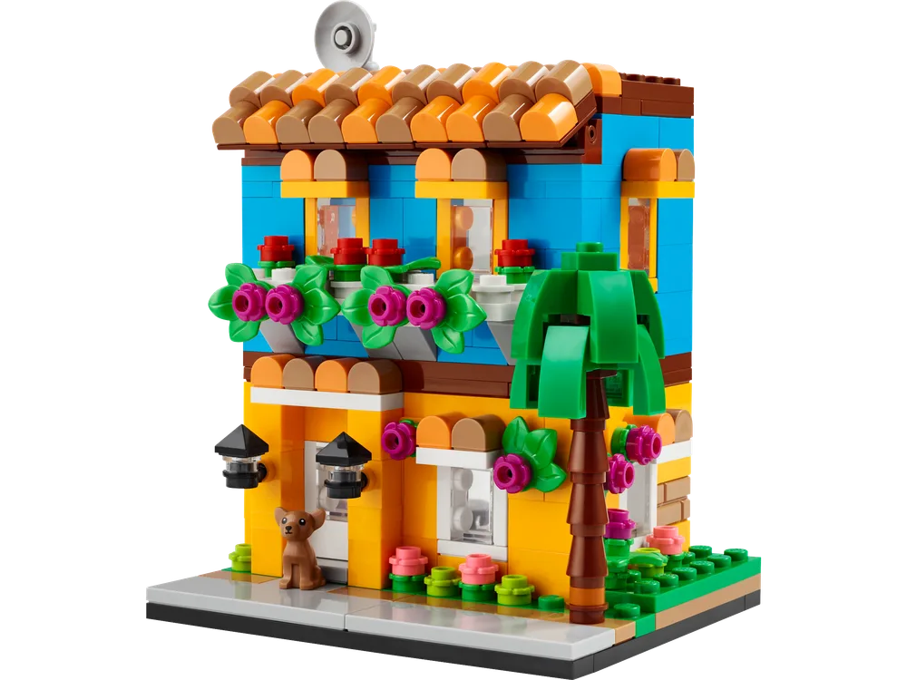 Front view of the vibrant blue and yellow LEGO house with a terracotta-tiled roof, featuring flower boxes, a small dog, and a palm tree.