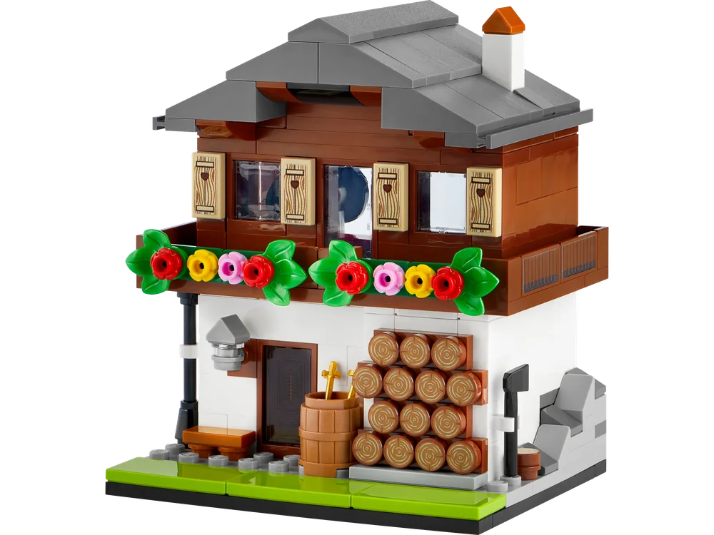 Front view of the LEGO 40594 Houses of the World 3, an Alpine house model with a brown upper floor, white lower floor, grey roof, green base, a decorated balcony, and a stack of logs.