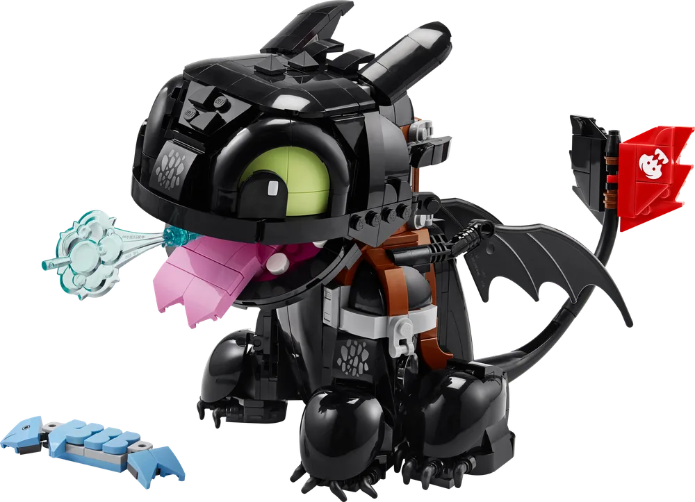 The LEGO Icons 10375 Toothless model, black with lime green eyes and a pink tongue, exhaling a trans-light blue plasma blast, with a blue brick-built fish accessory next to it.