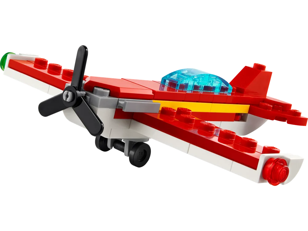 A close-up view of the small red, white, and yellow LEGO plane with a black propeller and trans-blue canopy, angled as if in flight, against a white background.