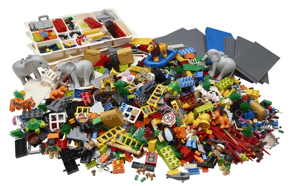 A large pile of assorted LEGO bricks, minifigures, animals including elephants and a tiger, baseplates, and a sorting tray full of smaller elements, all on a white background.