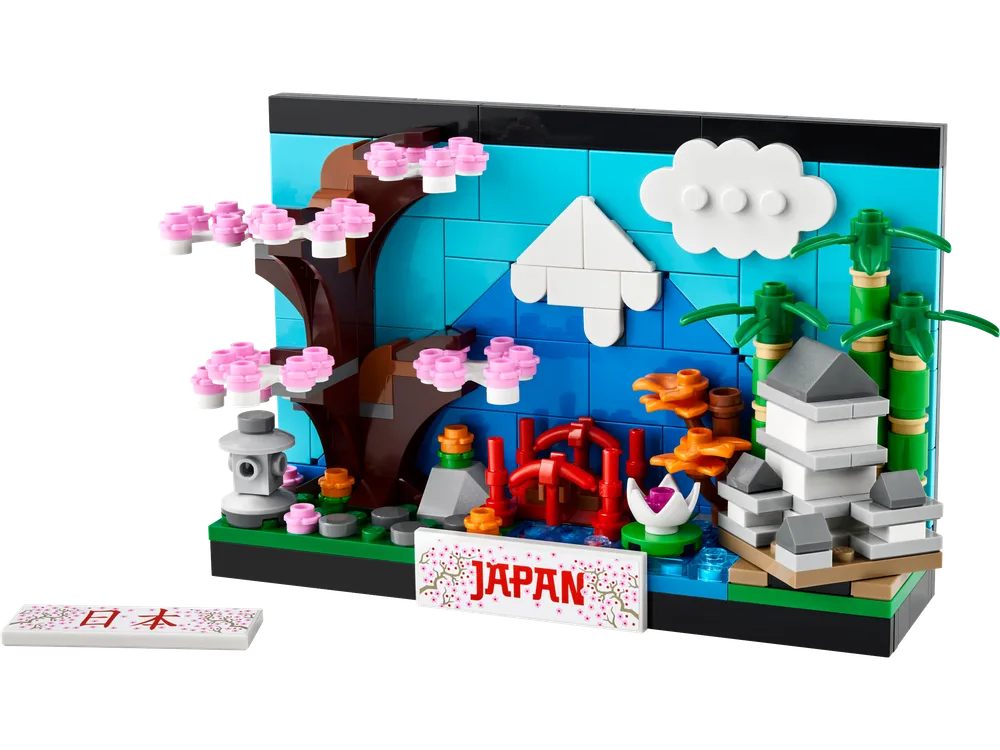 A detailed LEGO Japan postcard model with Mount Fuji, cherry blossoms, a torii gate, and a pagoda, next to a printed tile.