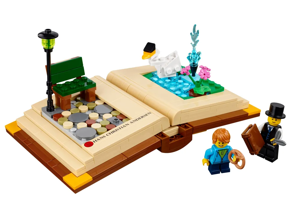 An open LEGO brick-built book features two scenes: a park with a bench and lamppost on the left, and a pond with a swan and fountain on the right. Two minifigures, an adult in a top hat and a child, stand next to the book.