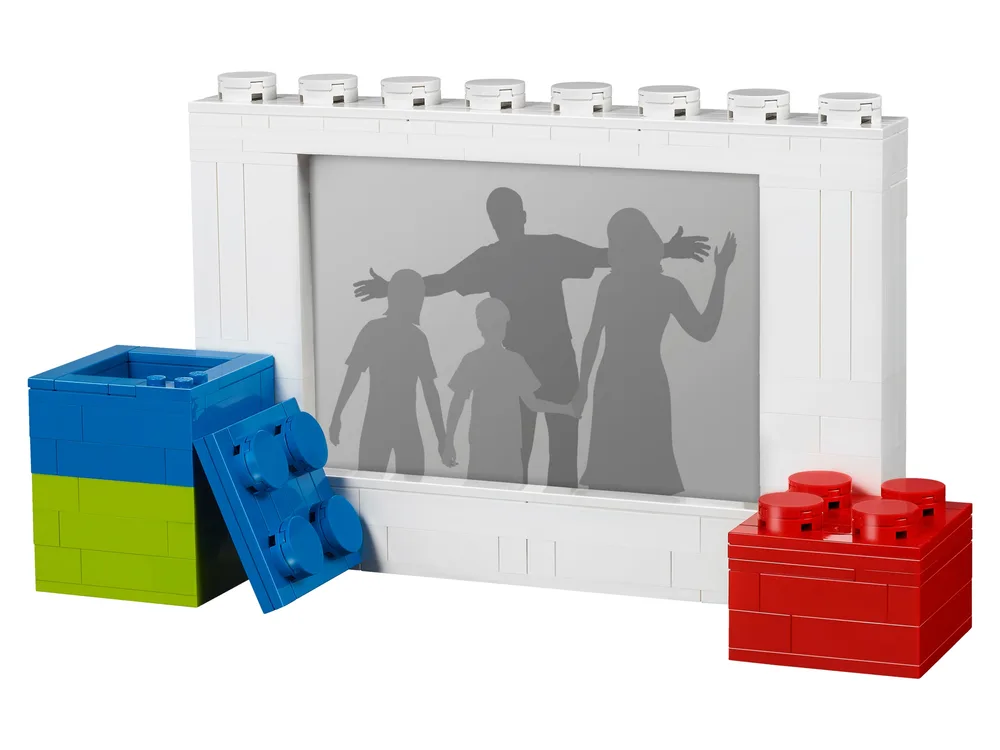 White LEGO brick-built picture frame holding a family silhouette photo, flanked by blue and lime green, and red LEGO storage bricks.