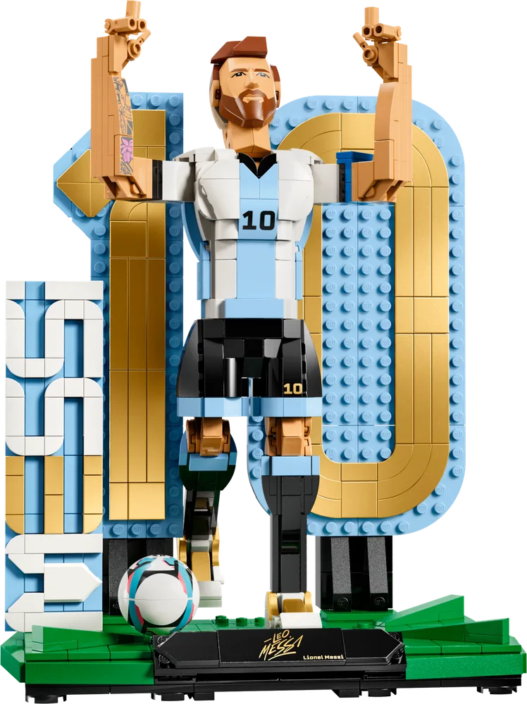 LEGO brick-built figure of Lionel Messi in a white and light blue jersey, number 10, with arms raised in celebration, standing on a green base next to a white and light blue "10" and "MESSI" sign. A soccer ball is at his feet.
