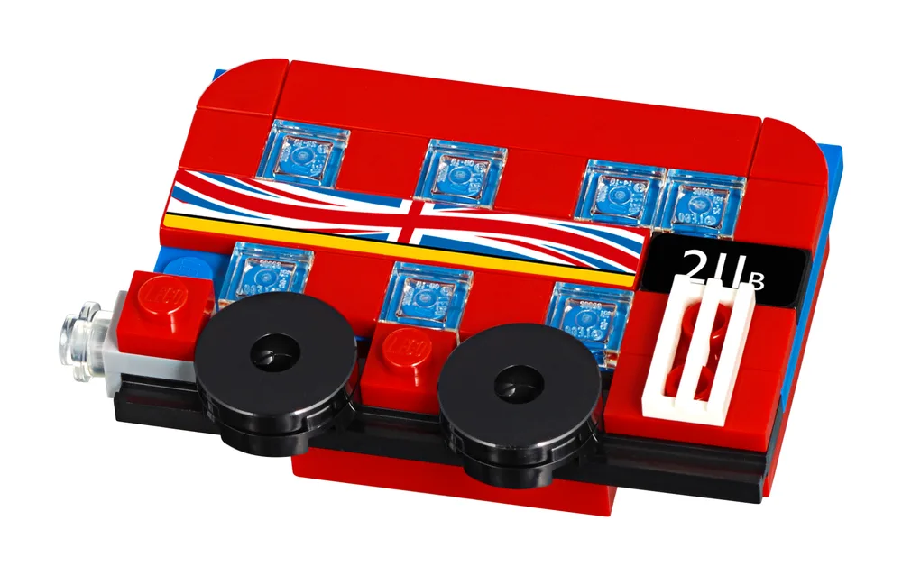 A detailed, angled close-up of a small, red LEGO London double-decker bus magnet with a Union Jack stripe along its side, clear windows, and black wheels, set against a white background.