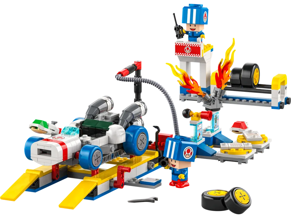A wide shot of the LEGO Super Mario™ Toad’s Kart and Garage set, featuring a white and red race car on yellow ramps, two blue-helmeted Toad mechanics, a tire rack with flames, and various garage tools.