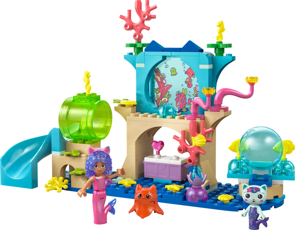 Full view of the LEGO Gabby's Dollhouse Mermaid Gabby's Ship and Spa set, featuring a blue base, tan archways, a central observation window, a green transparent tunnel, a slide, and three characters: Mermaid Gabby, Pandy Paws, and Baby Box Cat.