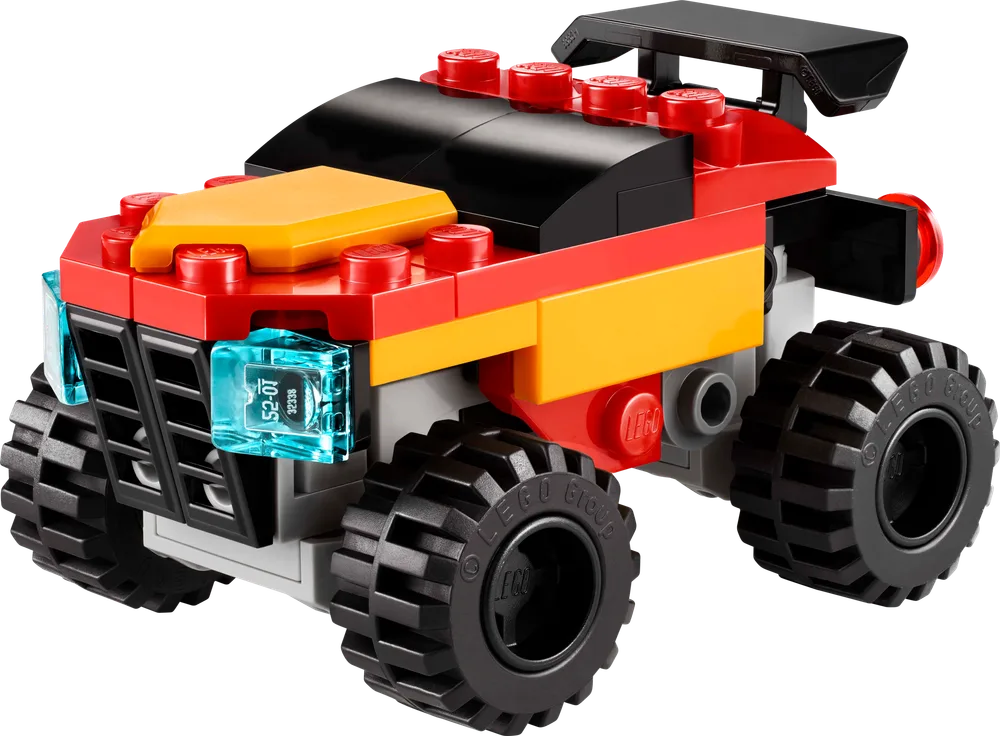A front three-quarter view of the small red, yellow, and black LEGO monster truck, featuring large black wheels and bright trans-light blue headlights.
