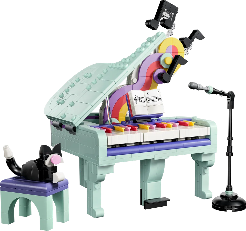 Close-up of a mint green grand piano made of LEGO bricks, featuring colorful keys, a music stand, and a small black cat sitting on a matching stool. A microphone on a stand is to the right.
