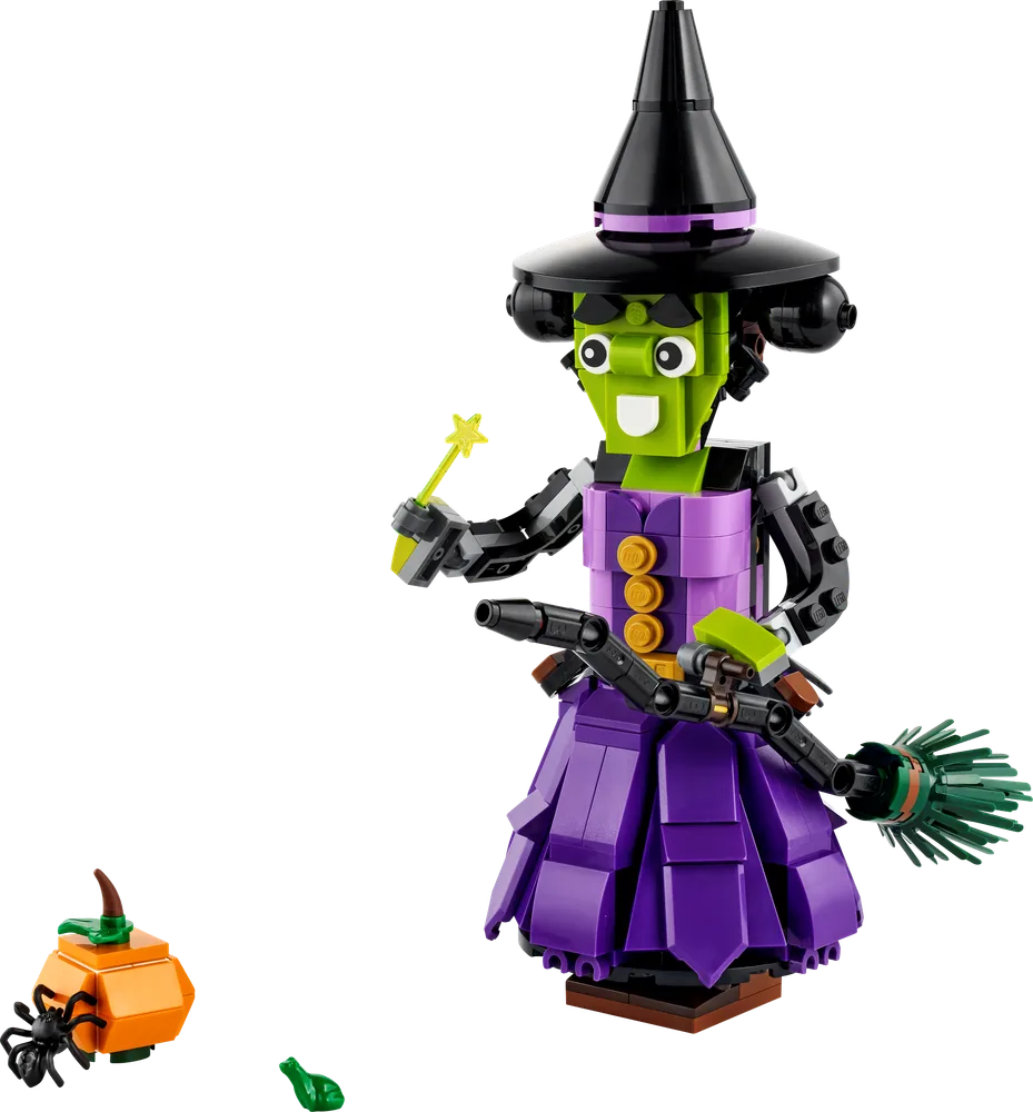 A brick-built witch figure with green skin, purple dress, and black hat holds a broomstick and a magic wand. A small orange pumpkin with a spider sits beside her.