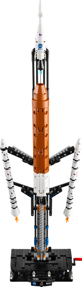 A tall, white, black, and orange LEGO Technic rocket model, the NASA Artemis Space Launch System, stands vertically on a black base with its launch support structure and detachable solid rocket boosters clearly visible.