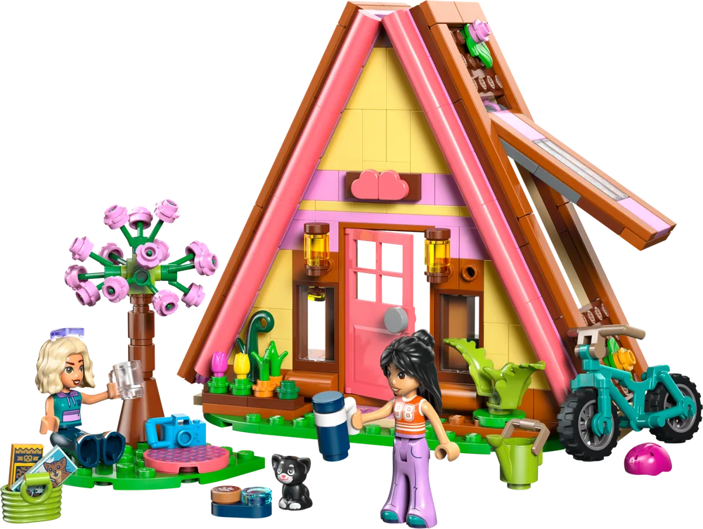 A fully assembled LEGO Friends Nature Glamping Cabin (Set 42682) is displayed, showing the A-frame structure, two minifigures, a cat, a bike, and a vibrant pink flowering tree, all on a white background.