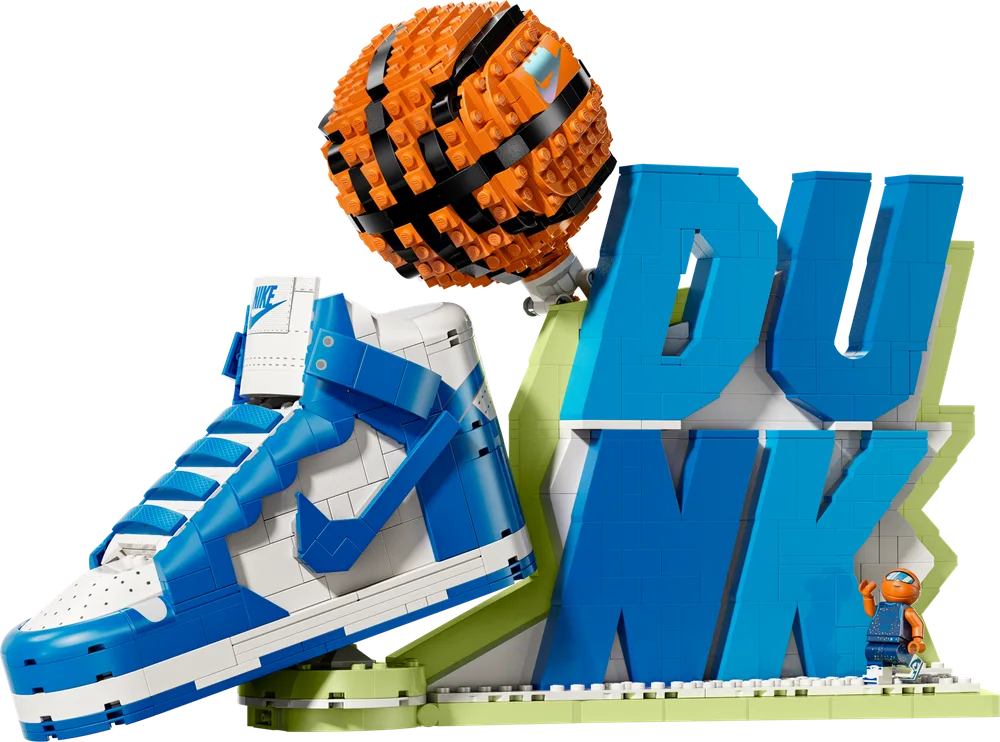 A dynamic display features a large, brick-built Nike Dunk shoe in blue and white, angled on a lime green base, alongside a similarly constructed 'DUNK' text sign and an orange LEGO basketball. A small minifigure stands near the sign.