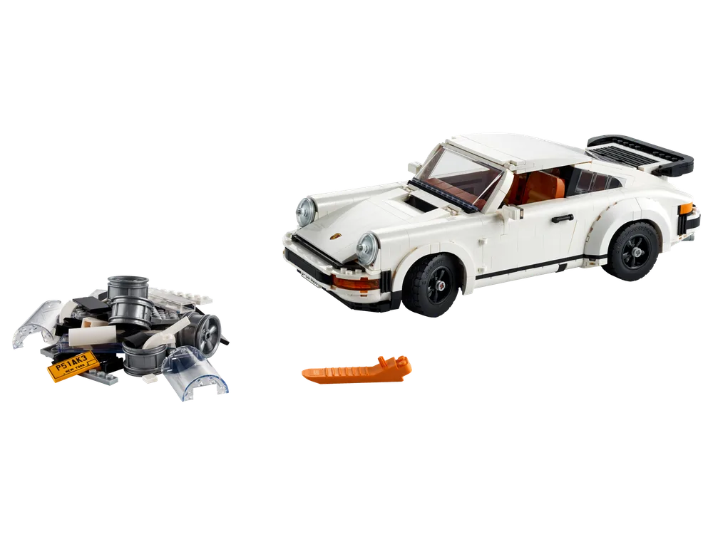 A white LEGO Porsche 911 Turbo model is displayed next to a pile of disassembled LEGO bricks that form a Targa roof and engine, against a white background.