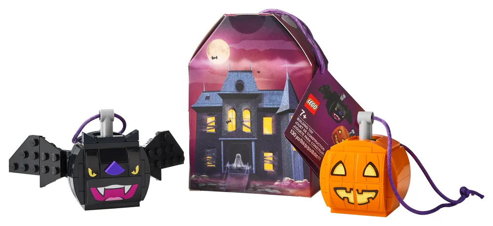Two Halloween-themed LEGO keychains, a black bat and an orange pumpkin, are displayed next to their haunted house-themed packaging box on a white background. Both keychains feature purple strings attached to a silver keyring element.