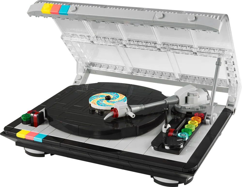 A LEGO Retro Record Player set, number 40699, is displayed with its clear plastic lid open, revealing a black turntable with a colorful record brick on top, and a detailed tone arm.