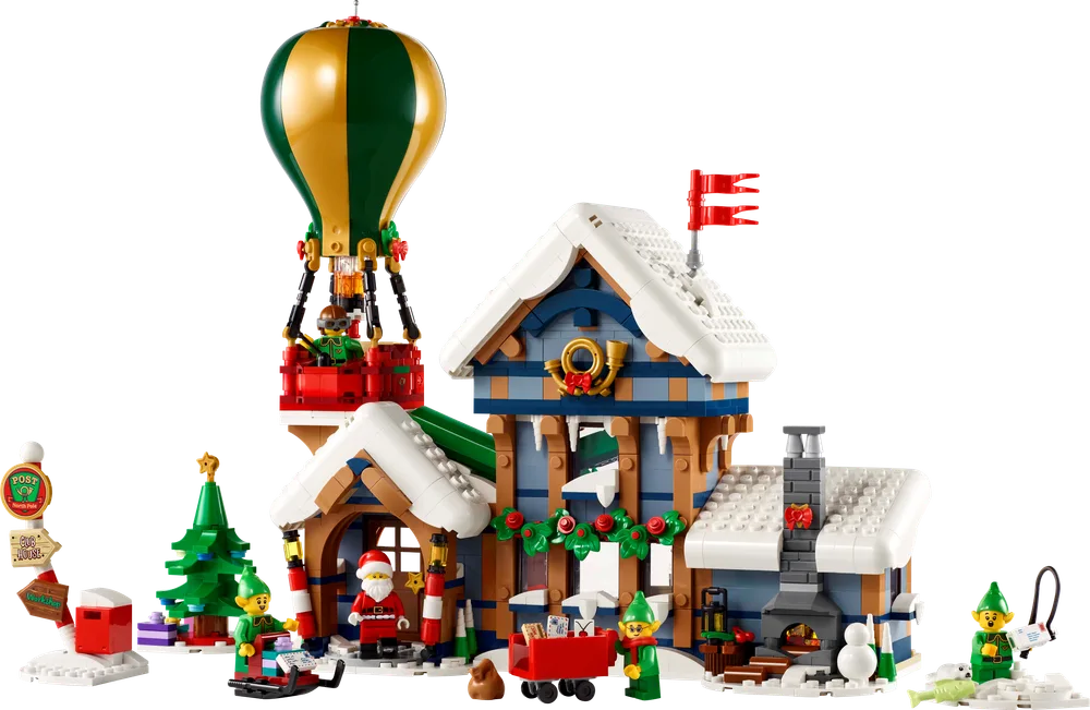 Full view of the LEGO Icons Santa's Post Office set 10339, featuring a two-story building, hot air balloon, Christmas tree, and minifigures, all covered in snow.