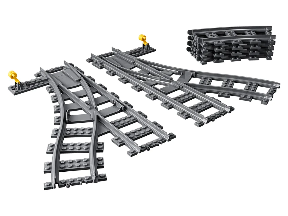 Two grey LEGO train switch tracks (left and right) are laid out, with a stack of four curved grey LEGO train tracks in the background on a white surface.