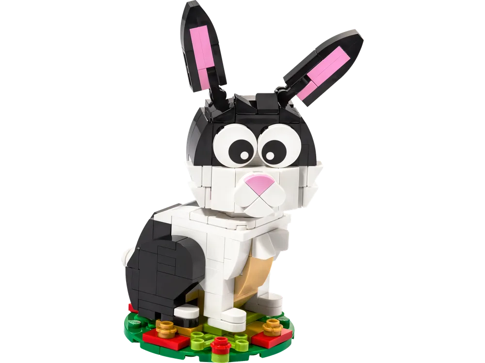 A black, white, and tan LEGO rabbit model with pink inner ears, standing on a green base with red and yellow accents.