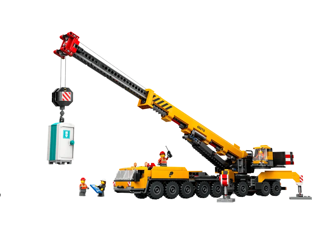 A bright yellow LEGO mobile crane in action, lifting a white and teal portable toilet, with three construction worker minifigures on the ground.